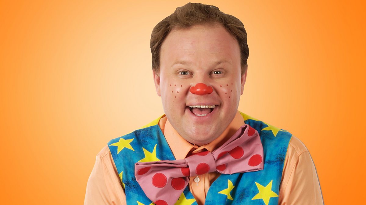 Justin Fletcher dressed up as Mr Tumble clown with orange background